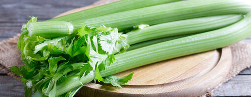 Fresh green celery stems on wooden cutting board